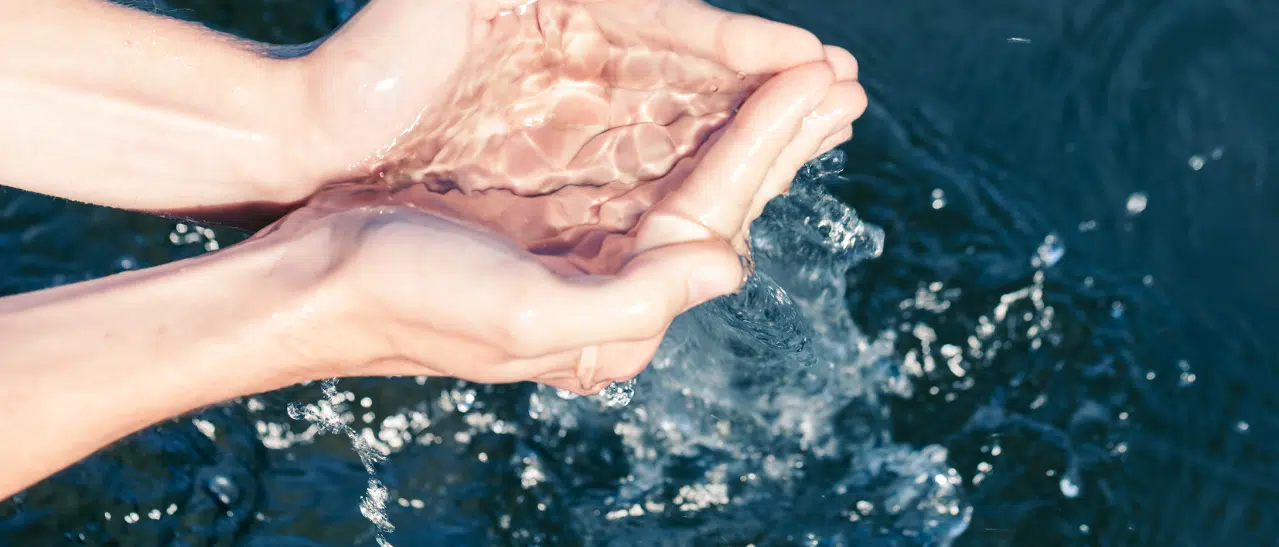 Frau schöpft kristallklares Wasser aus See, Symbol für nachhaltigen Umgang mit Wasserressourcen.