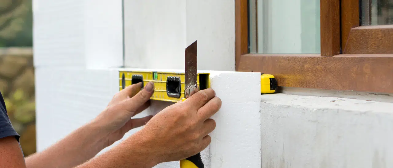 Handwerker misst und schneidet Fassadenplatten für Vollwärmeschutz präzise zu.