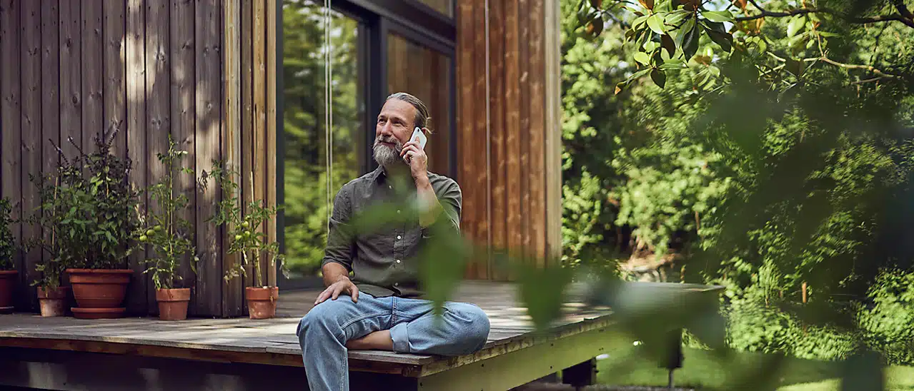 Glücklicher Mann sitzt vor seinem umweltfreundlichen Haus mit nachhaltigen Fenstern und Türen.