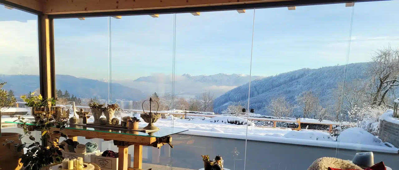 Ausblick von Terrasse mit Glasschiebewänden auf verschneite Landschaft in Oberösterreich.